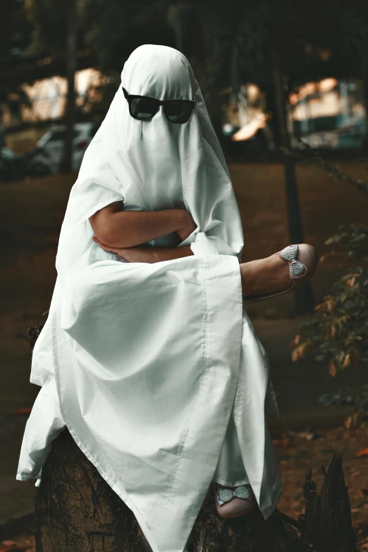 a person in a nun outfit sits on a stump in the woods