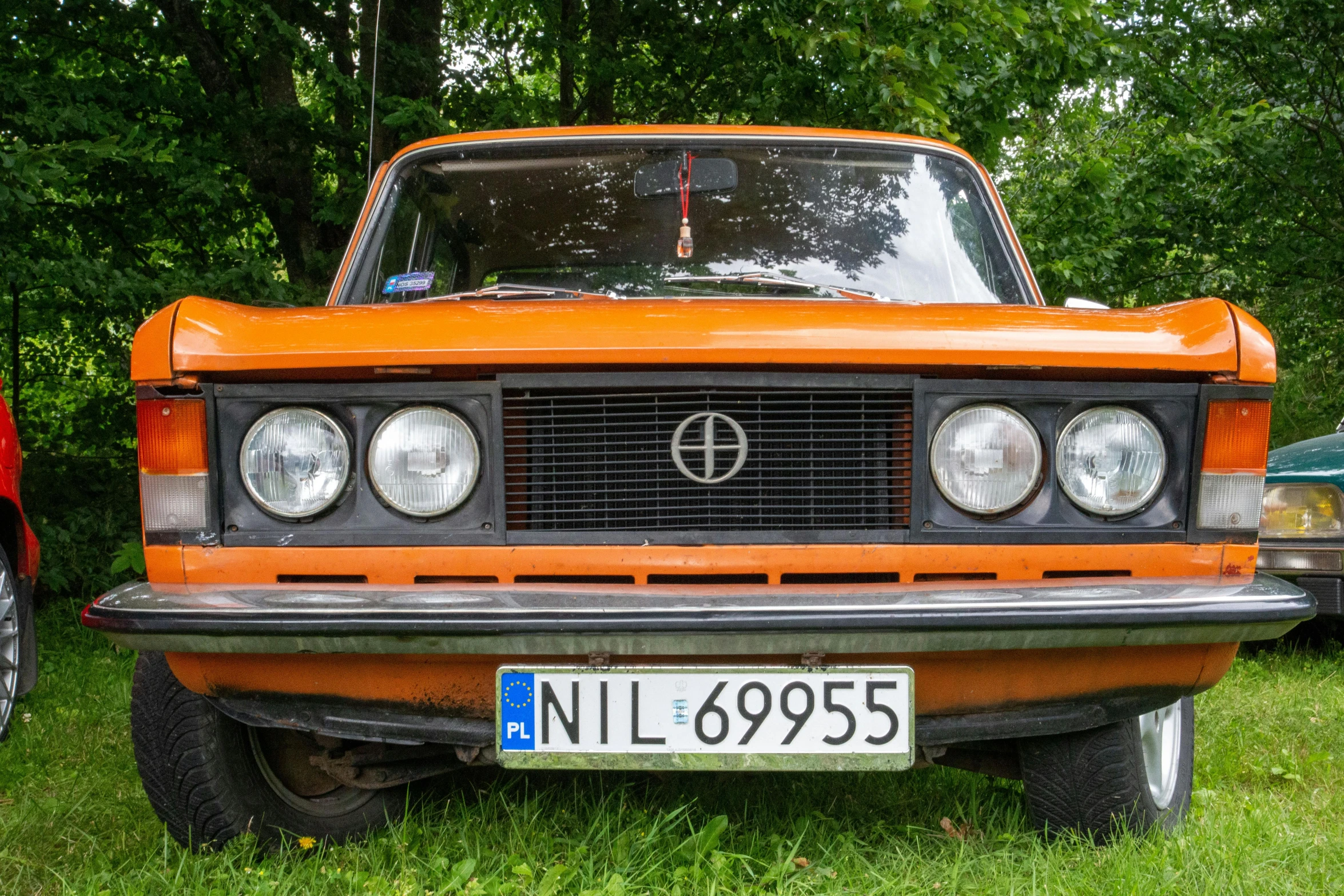 an orange car sits on the grass and is parked next to other cars