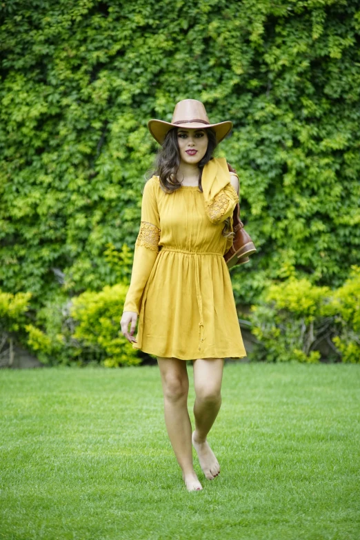 woman in yellow walking across grass with a hat on