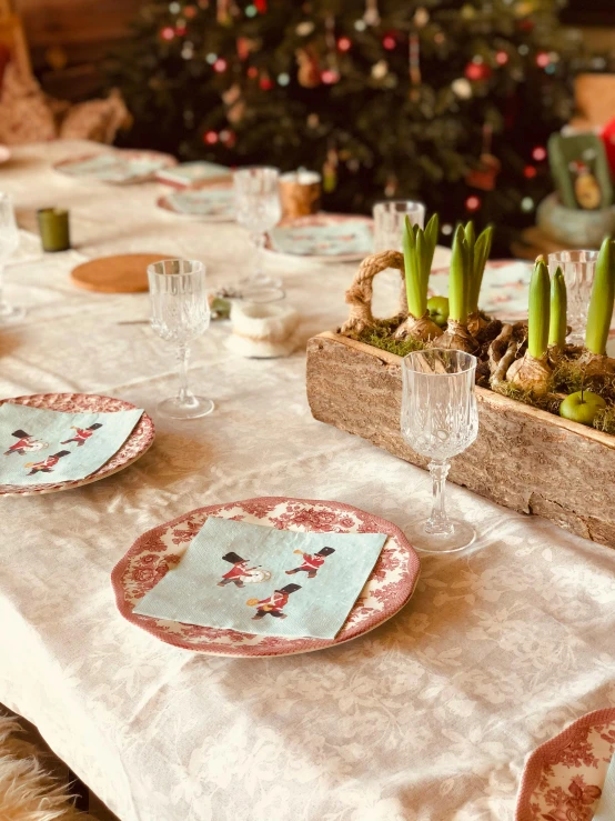 a wooden crate with flowers and plants is sitting on a table with dishes, cups and glasses