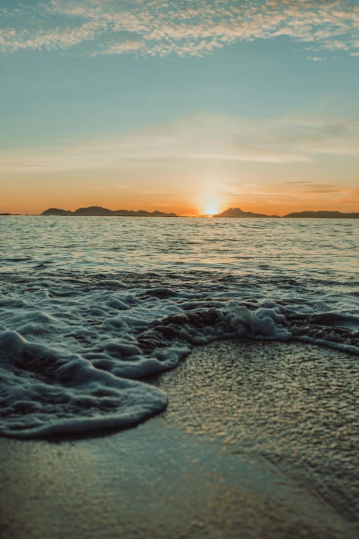 the sun rising over the ocean with waves coming in