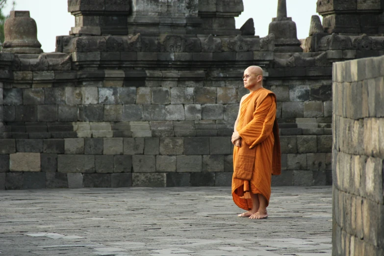 monk in orange robe stands in front of a line of stone structures