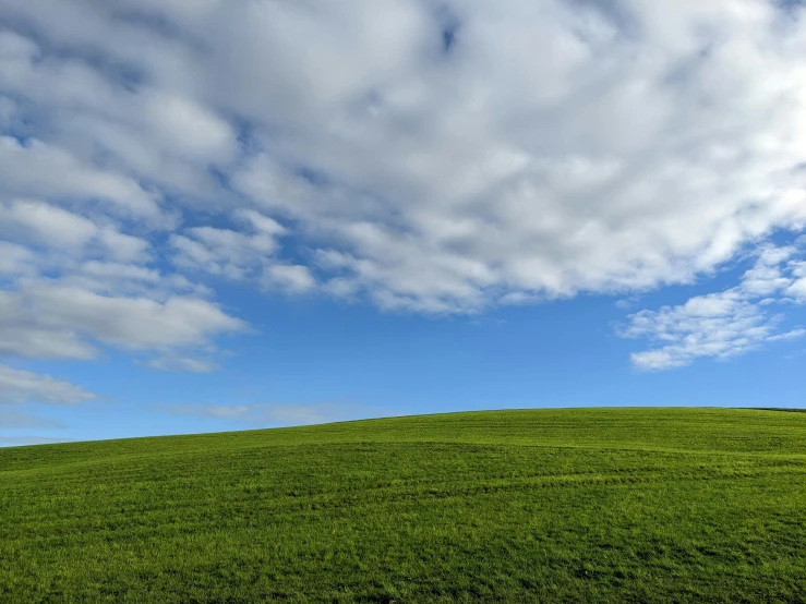 an open grassy field with clouds and a bench