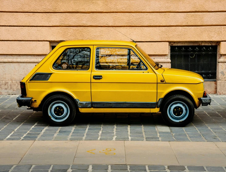 a small yellow car parked by the side of a building