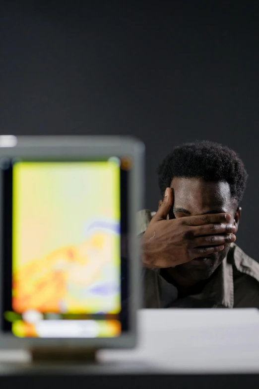 a man covers his face next to a computer monitor