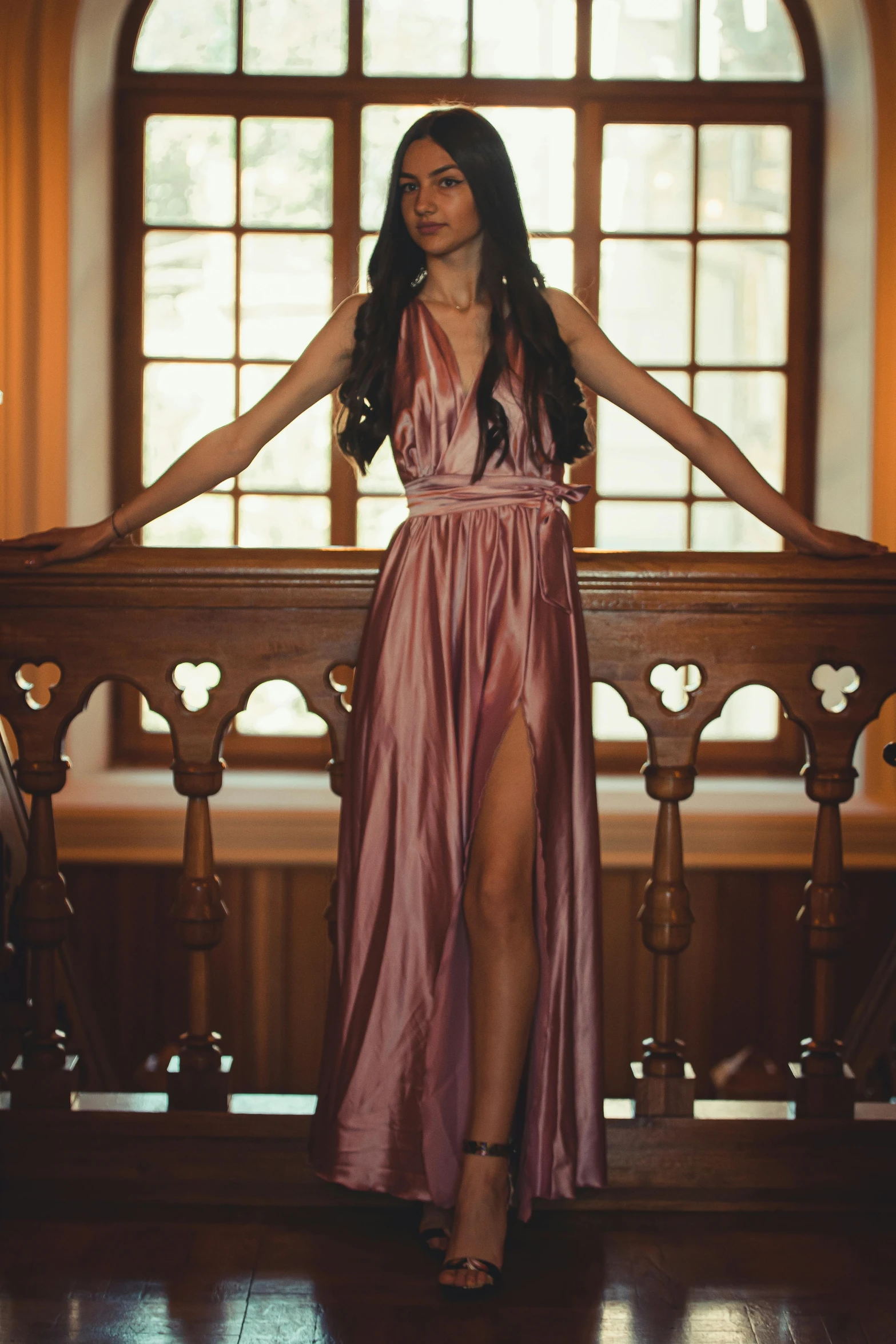 a woman wearing a long dress stands in front of an arched window