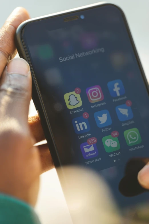 a hand holding a cell phone with various social icons on the display