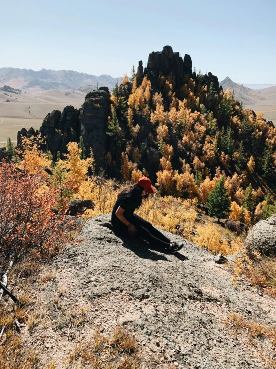 a person sitting on a large rock near some trees