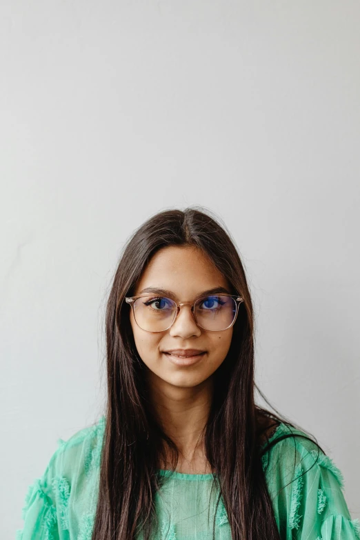 a woman with glasses and green blouse standing in front of a wall