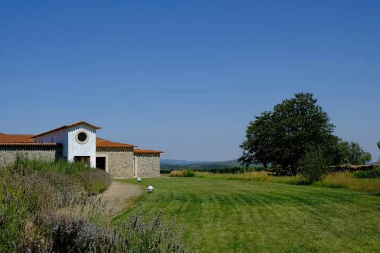 a stone house with an orange roof sitting on the side of a lush green field