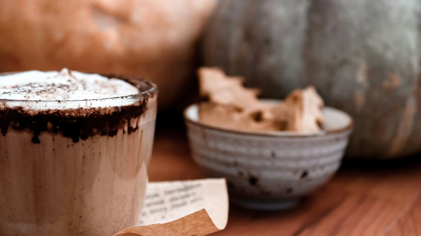 the cinnamon topped drink is on the wooden table next to decorative pumpkins