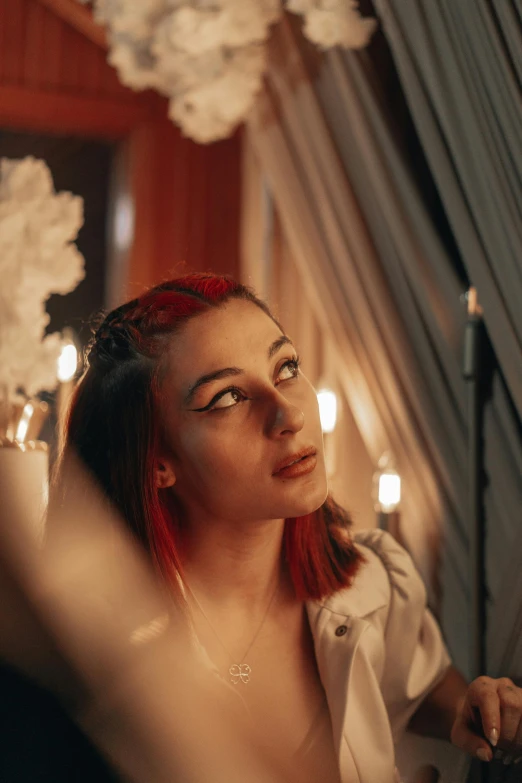 a woman with red hair in white jacket holding candle with wall