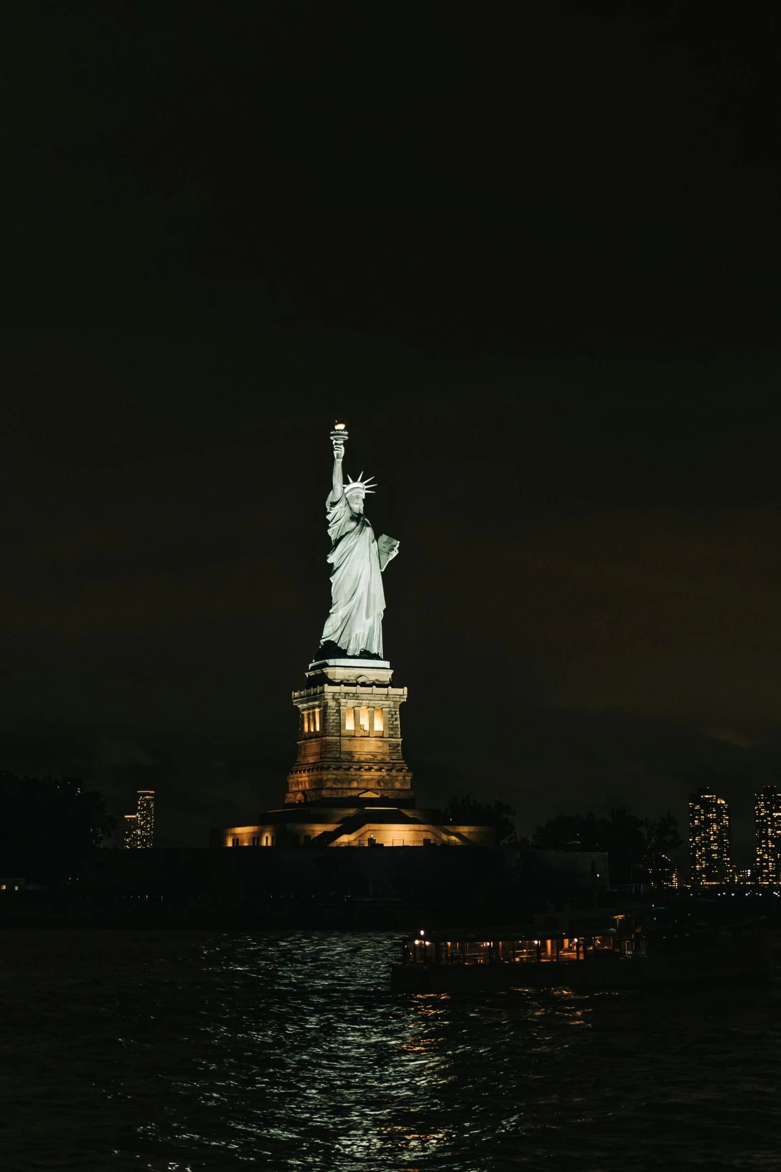 a statue of liberty on the water with lights reflecting off its sides