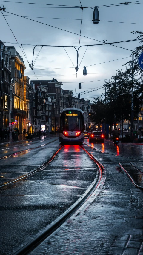 a city street that has rain, street lights, a train engine and some cars