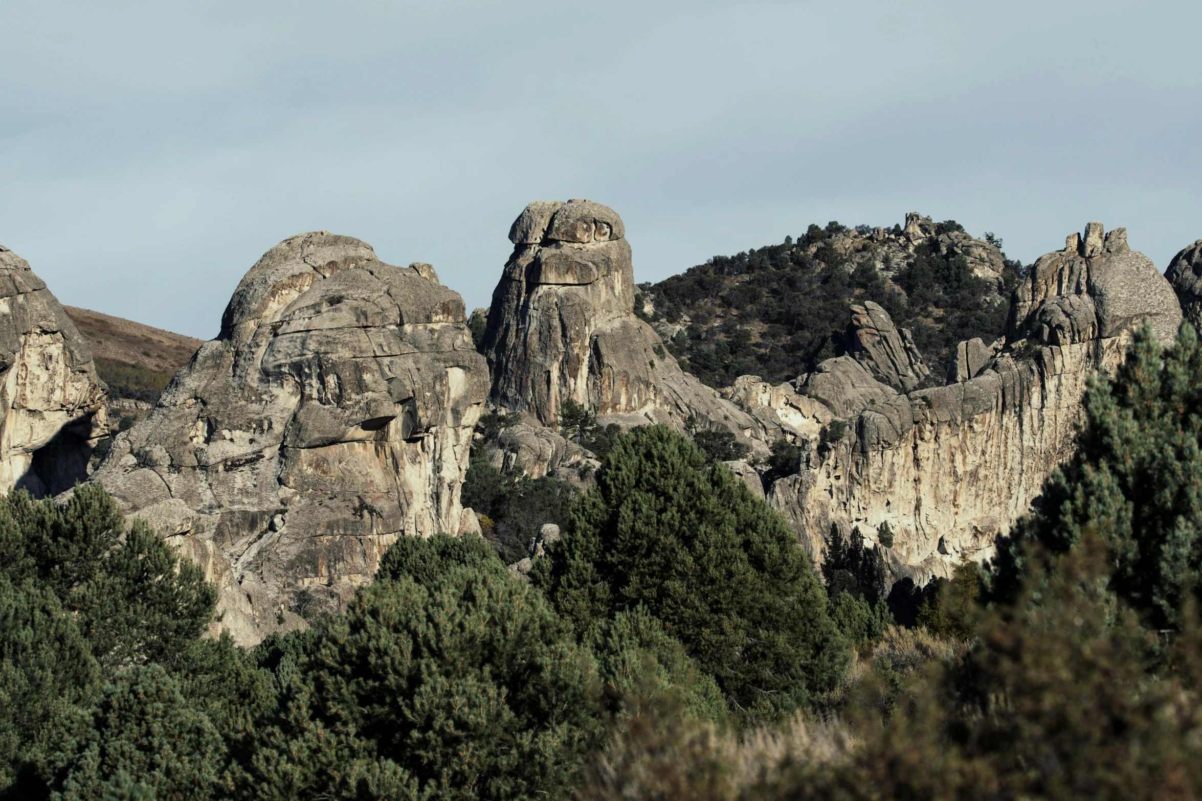 rocky landscape with several peaks and trees under a partly cloudy sky