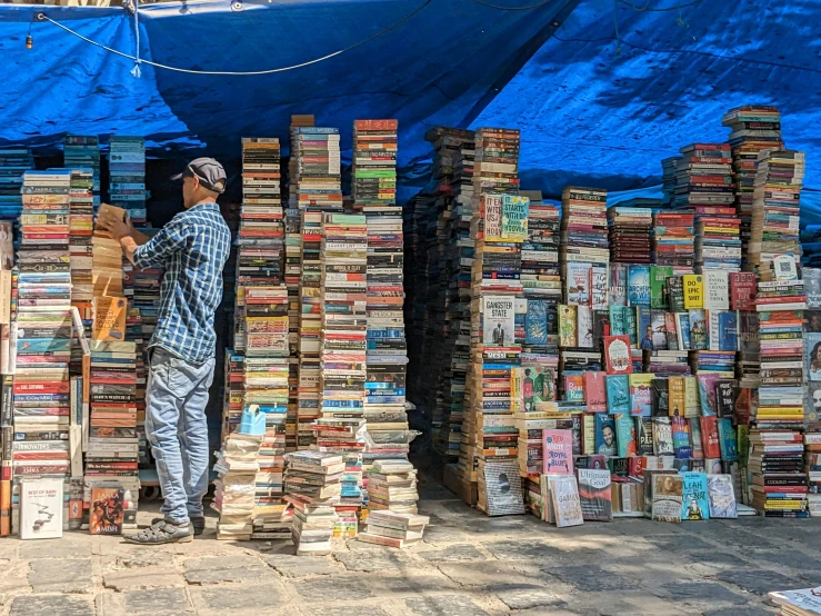 man picking up a large pile of books from a book market