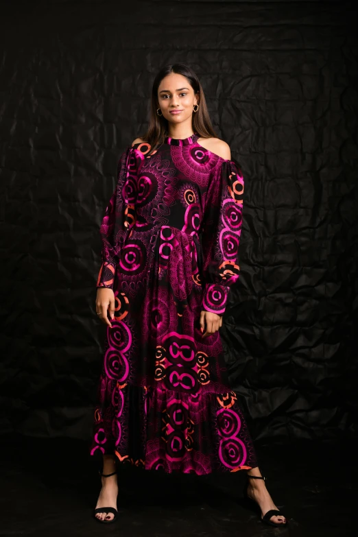 woman standing on black surface wearing a purple gown with pink and gold print