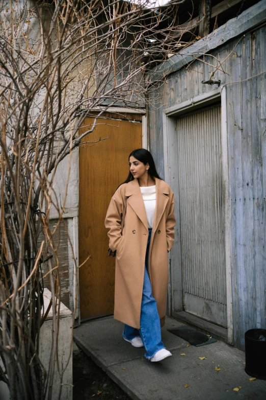 a woman standing next to a door wearing a tan coat