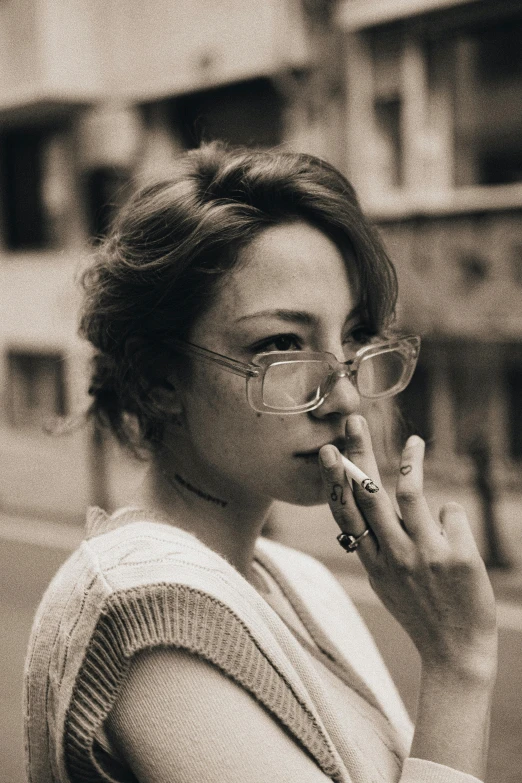 a woman smokes a cigarette outside while wearing glasses