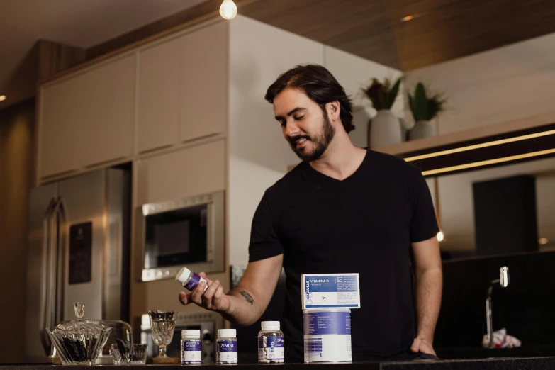 a man standing in a kitchen holding a bottle and a spoon