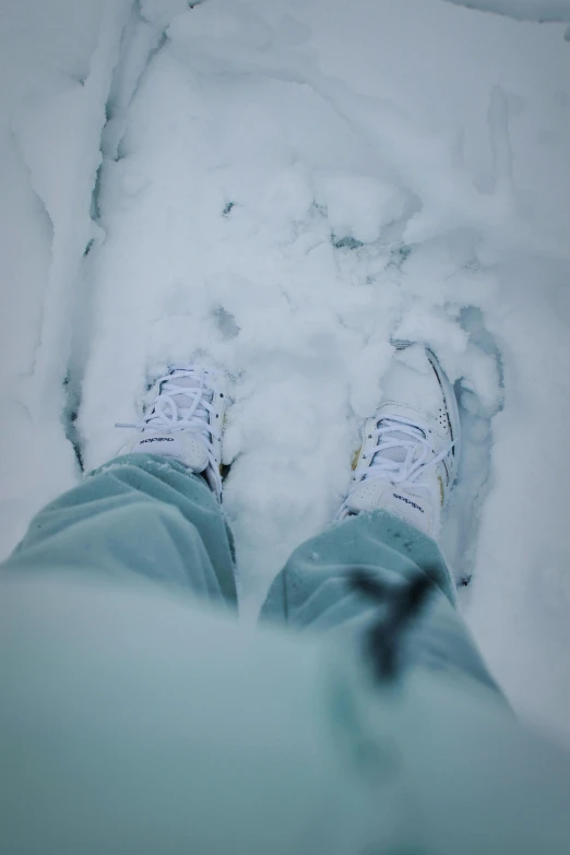 someone standing with their feet in the snow wearing white and blue sneakers