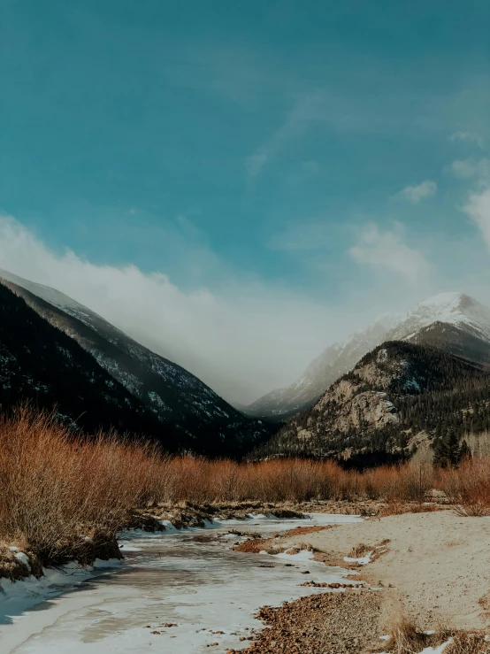 there are snowy mountains in the distance and snow in the grass in the foreground