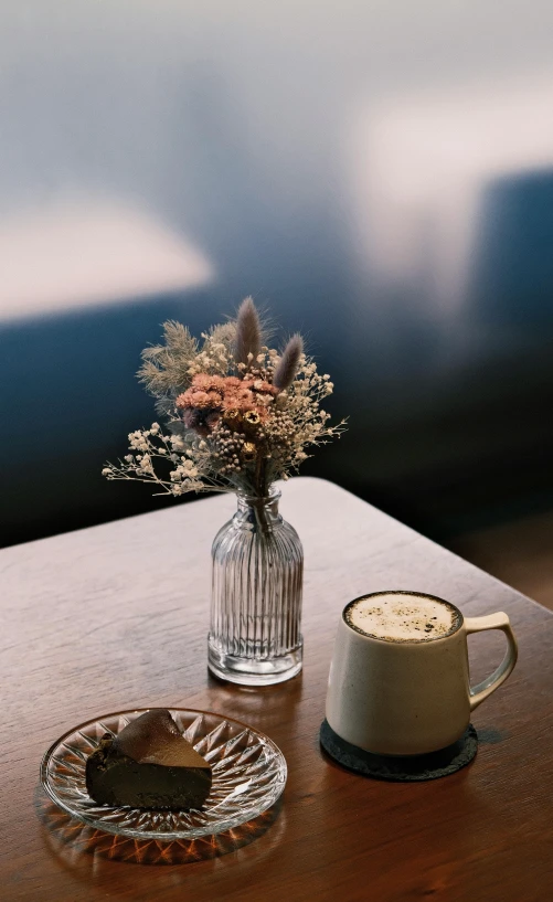 coffee cup and glass vase on a table with small plate