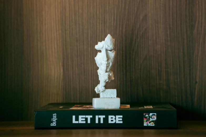 a white statue stands on top of a black book