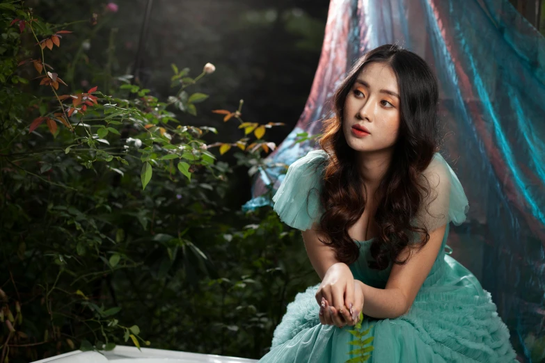 an asian girl dressed in green sits on a chair outdoors