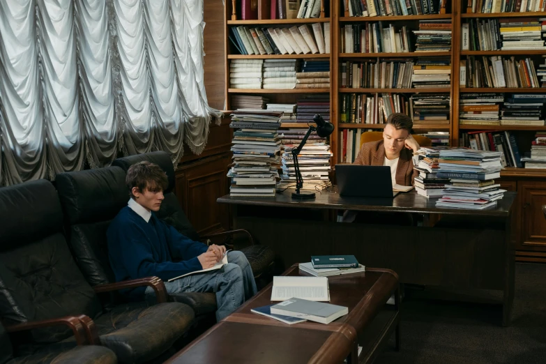 two people at a table with a laptop and book on it in a liry