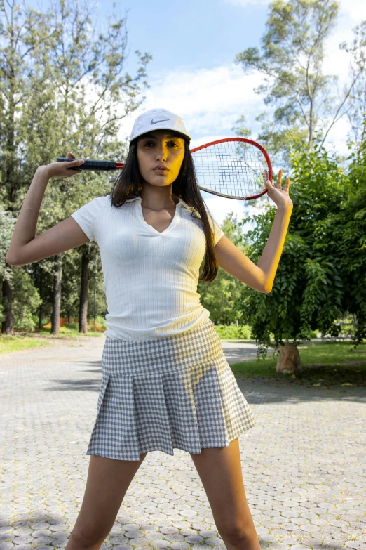 a woman poses in tennis attire while holding a tennis racket