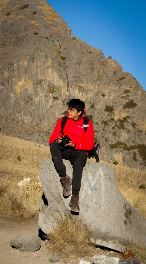 man in red jacket on rock and mountainside looking