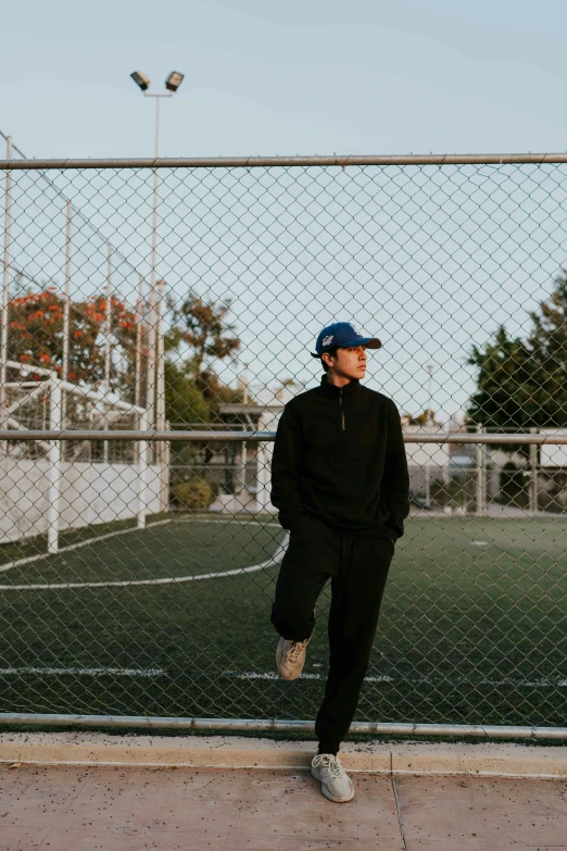 a man standing on a soccer field, with a baseball cap on and one leg in the air