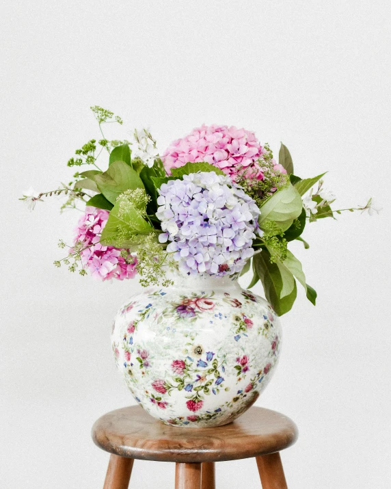 a floral vase sitting on top of a wooden stool