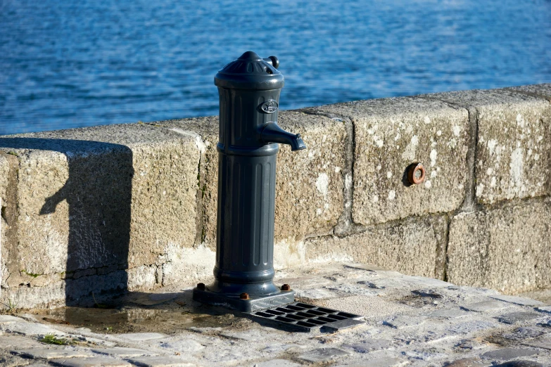 a parking meter next to a stone wall and water