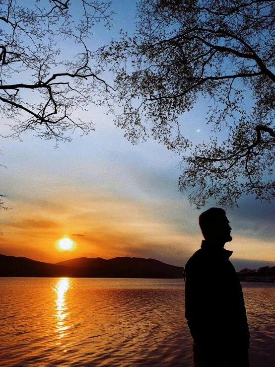 a man is standing in the sunset looking at the water