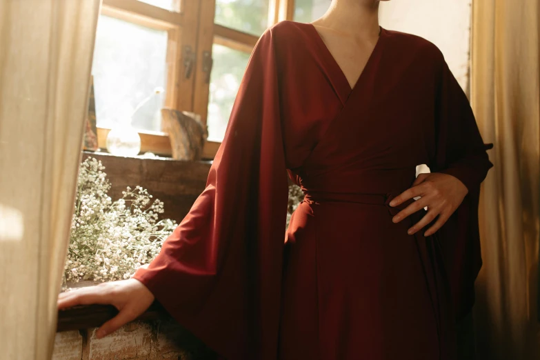 a woman in a red dress is standing near a window