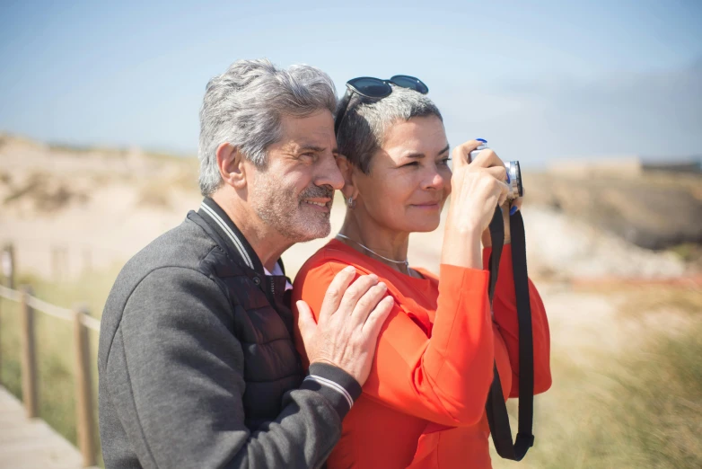 an older couple holding a camera on the side of a road