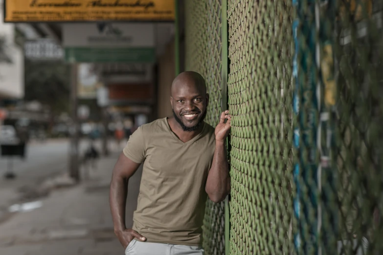 a smiling man with a tan shirt leaning against a fence