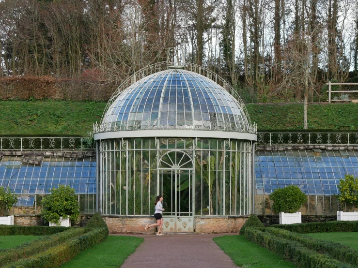 a woman standing inside of a glass building in a garden