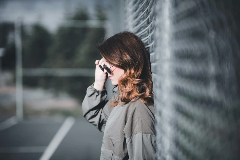 the woman is standing near a fence, holding her ear