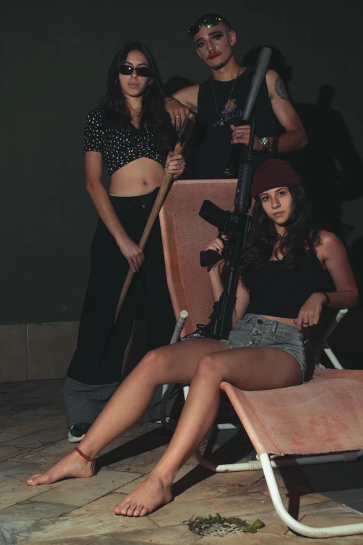 a group of young people sitting around one another and one is holding a gun