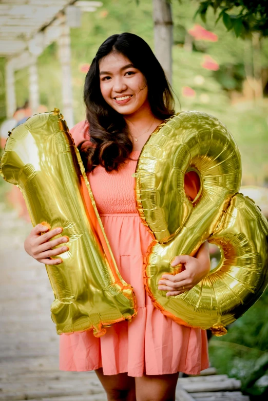a woman in a pink dress holding balloons in the shape of the number twenty
