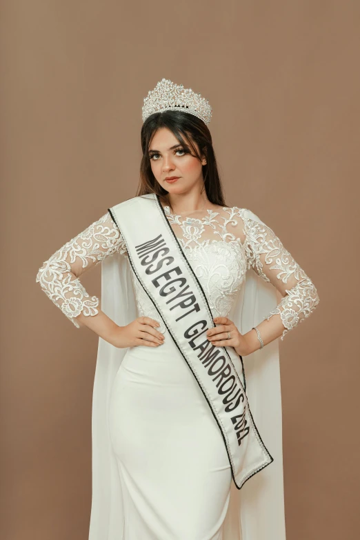 a woman in white is standing on the side of a brown wall wearing a crown and holding