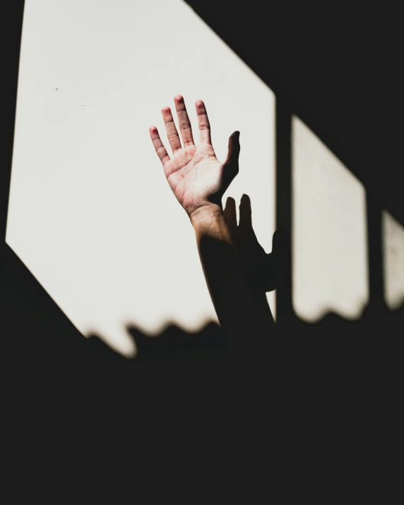 person's hands reach towards the sunlight on the wall