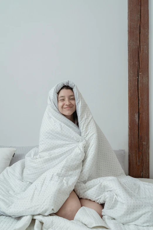 a girl wrapped in bed while smiling at the camera