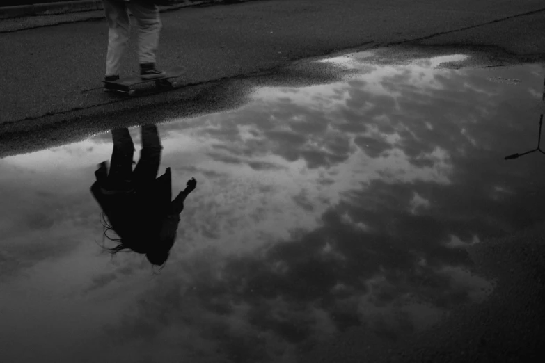 a skateboarder is standing on the side of a street with his reflection in water