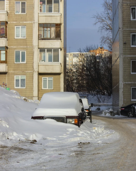 a snow plow moving across a snowy road in front of apartment buildings