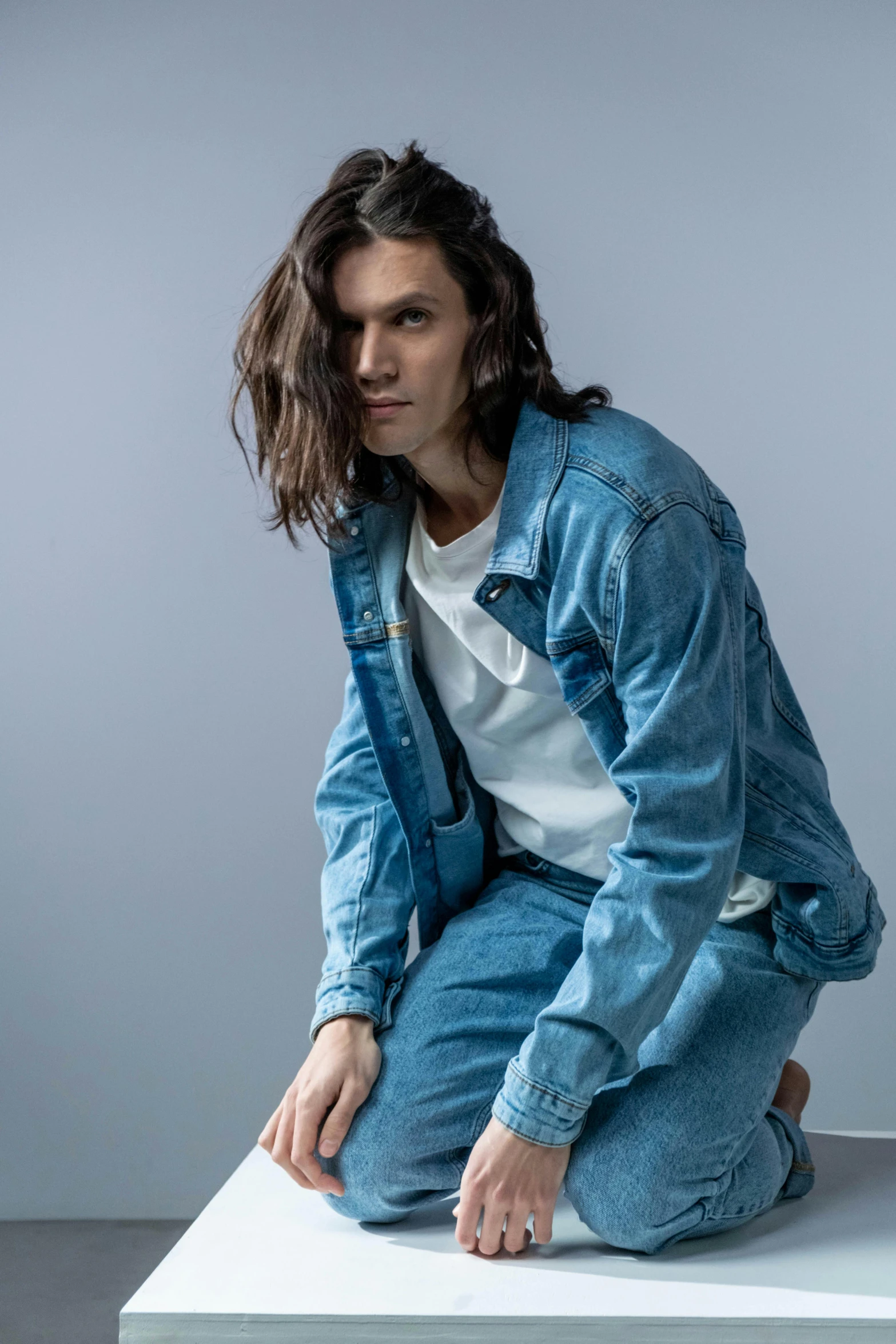 young man with dark hair and blue jean sitting on top of a table