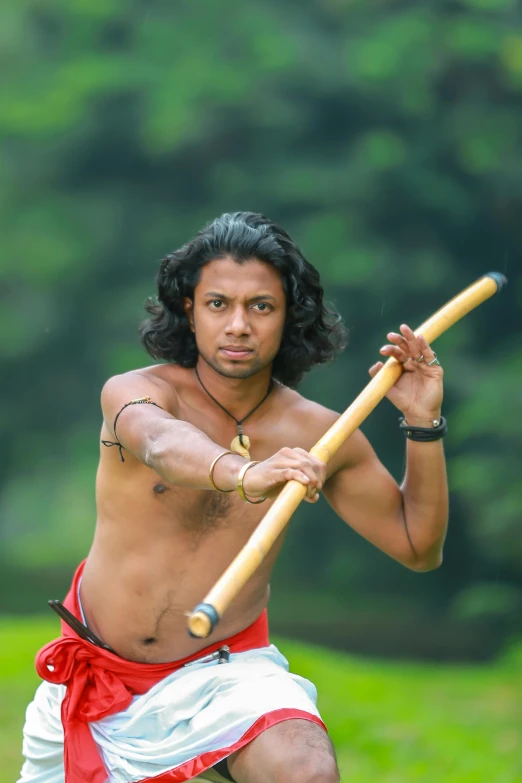 a man in the grass holding a wooden stick